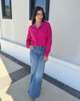 Woman wearing a pink shirt and blue jeans standing outside a building.