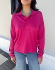 Person wearing a bright pink long-sleeve shirt and blue jeans against a neutral background, close up, untucked