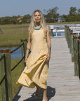 Woman in a yellow dress and Cely Sandals standing on a wooden boardwalk with a scenic background
