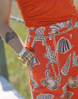 Person wearing a red patterned skirt with a gold chain and gold ring, standing outdoors.