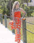 Woman in an orange outfit standing on a wooden bridge with greenery in the background