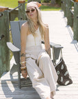 Woman in a white outfit sitting on a wooden deck with a black bag.