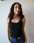 Woman wearing a black tank top and blue jeans against a plain background