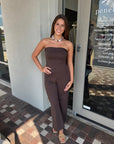 Woman in a brown strapless jumpsuit standing outside a store.