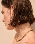 Close-up of a person wearing a gold chain necklace against a beige background