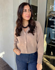 Woman wearing a beige cardigan and blue jeans standing outside a store.
