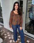 Woman wearing a patterned blouse and jeans standing outside a store.