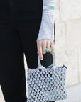Person wearing black pants and a patterned top, holding a small gray handbag.