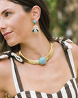 A close-up lifestyle shot of a woman wearing a gold-toned choker necklace with a round turquoise stone and matching drop earrings with turquoise, white, and gold feather-like details.