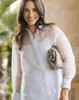 A woman wearing a blue sheer long-sleeve button-up shirt matching skirt, holding a snakeskin-patterned crossbody bag.