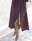 Person wearing a long burgundy dress with a high slit and leopard print boots on a stone pavement.