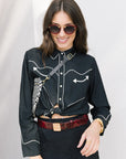 Woman wearing the western shirt with black outfit with white accents and sunglasses against a plain background