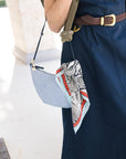 detail of Aila choco leather belt on a model with a blue dress and green sweatshirt over her shoulders holding a blue bag with a scarf tied to it