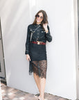 Woman wearing the western shirt with black outfit with white accents and sunglasses with a lace black skirt against a plain background