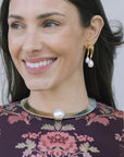 model wearing a floral top with a two tone necklace with a large pearl at the center with gold earrings that have a double pearl drop