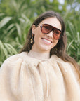 model wearing tortoise sunglasses and a tan fur cape that ties at the neck, close up