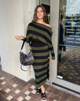 Woman in a green and black striped dress standing outside a store.