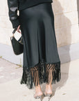 model wearing a black skirt with fringe at the bottom and snake print heels, back view