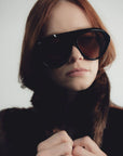 Person wearing dark sunglasses and a fur coat against a plain background