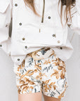 Person wearing a white jacket with floral patterns and floral shorts on a light background