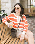 Woman in a striped sweater sitting on a bench holding a drink.