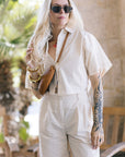 Person wearing a white outfit with sunglasses and a handbag, standing outdoors.