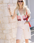 Woman in Liset One Piece and denim Bermuda shorts standing against a stone wall.