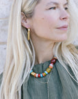Woman wearing a colorful beaded necklace and gold hoop earrings against a neutral background
