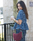Woman holding a coffee cup with a maroon handbag, standing against a stone wall.