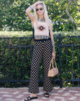Woman in a sleeveless top and polka dot pants standing outdoors with greenery in the background
