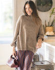 Woman wearing a brown sweater and striped pants in a kitchen setting