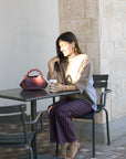 Woman sitting at an outdoor cafe table with a red handbag and a cup.