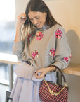 Woman holding a checkered handbag with floral embellishments on a blurred indoor background