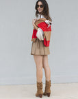 Woman wearing a red and beige color-blocked sweater with a beige skirt and brown boots against a light gray background.