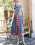 Woman wearing a graphic t-shirt and patterned skirt standing outdoors.