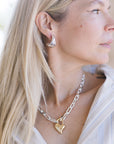 Close-up of a person wearing a gold heart-shaped necklace and silver earrings.
