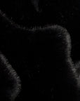 A close-up of black faux fur fabric with soft, textured strands and curved edges.