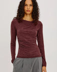 model wearing a long sleeve merlot top with a cowl neck and grey pants on a light grey background