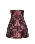 A strapless structured mini skirt in a deep burgundy brocade fabric with an intricate floral pattern in pink, red, and green, shown against a plain white background.