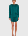 A model wearing a dark teal green long-sleeve mini dress with a gathered, pleated design, paired with brown pointed-toe heels, against a solid light gray background.