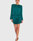 A model wearing a teal green off-the-shoulder long-sleeve mini dress with ruched detailing, paired with brown pointed-toe heels, against a solid light gray background.
