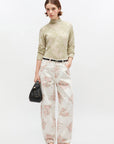 Woman wearing a light green sweater and floral pants with a black handbag on a white background