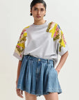 Woman wearing a grey sweatshirt with colorful sleeves and a denim skirt on a light background