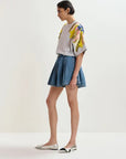 Woman wearing a floral embroidered top and denim skirt on a white background