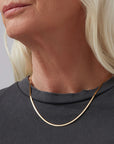 Close-up of a person wearing a thin gold necklace against a neutral background
