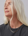 Person with blonde hair wearing a dark shirt and gold necklace against a gray background