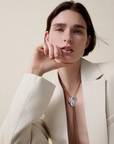 Woman wearing a beige blazer and a necklace with a bird design on a neutral background