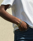 Person wearing a gold bracelet on a neutral background