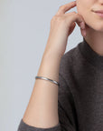 Person wearing a silver bracelet on a plain background
