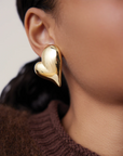 Gold heart-shaped earring worn by a person with a blurred background